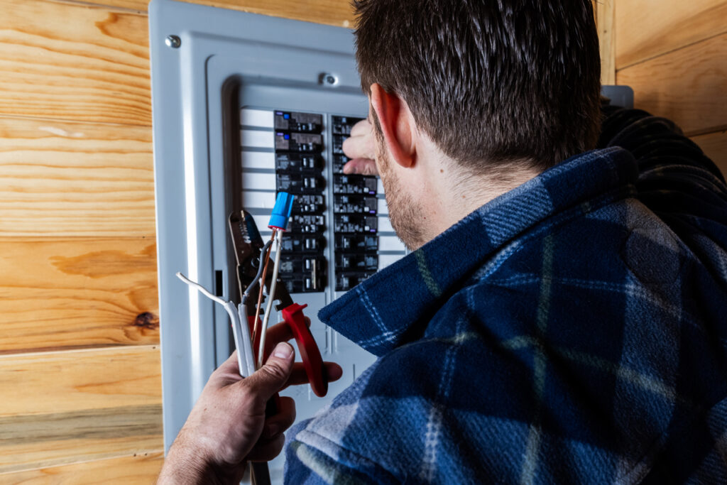 Tradesperson wiring a circuit breaker panel, holding wire cutters and insulated conductors.