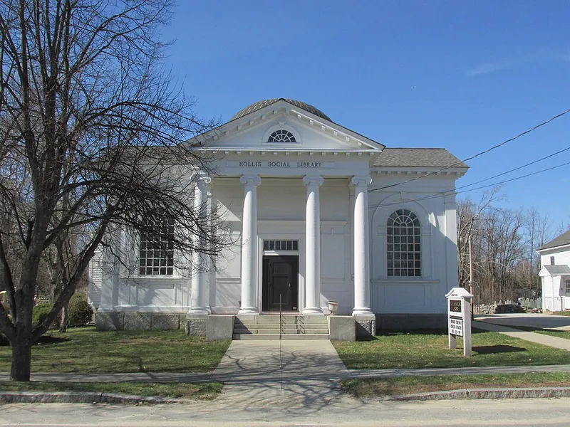 Front view of Hollis Social Library: white neoclassical building with four columns and a domed roof, on a sunny day.