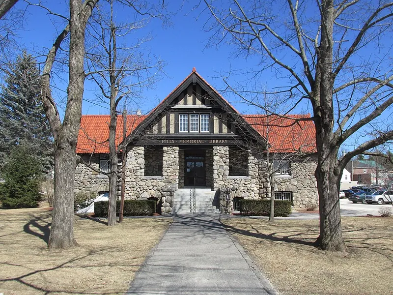 Stone library with a stone facade and red gabled roof, centered entrance, and bare trees framing a path leading to the door.